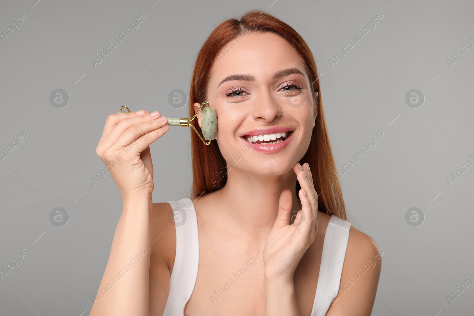 Photo of Young woman massaging her face with jade roller on grey background