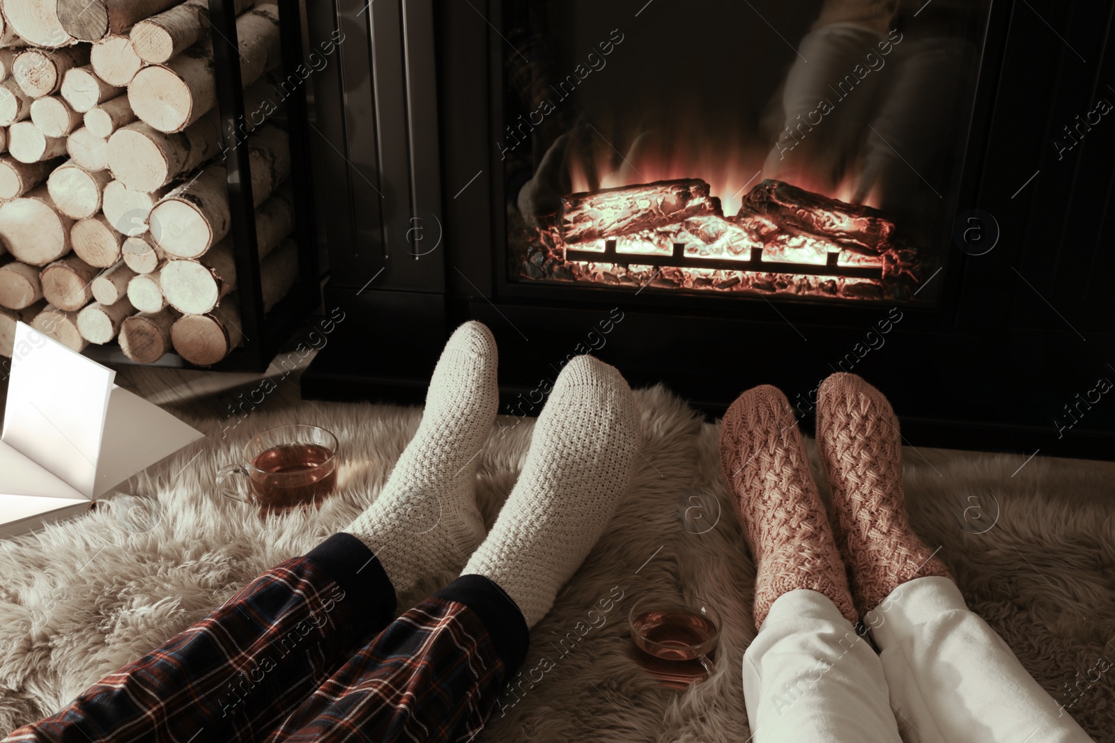 Photo of Couple in knitted socks near fireplace at home, closeup of legs