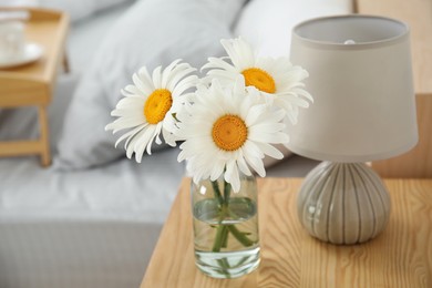 Bouquet of beautiful daisy flowers and lamp on nightstand in bedroom