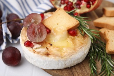 Photo of Tasty baked camembert with crouton, grape and rosemary on white tiled table, closeup
