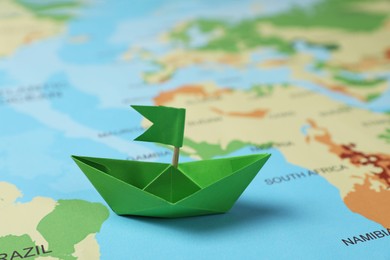 Photo of Green paper boat with flag on world map