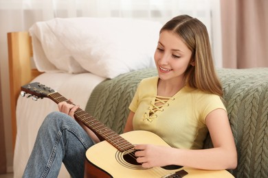 Teenage girl playing acoustic guitar near bed in room