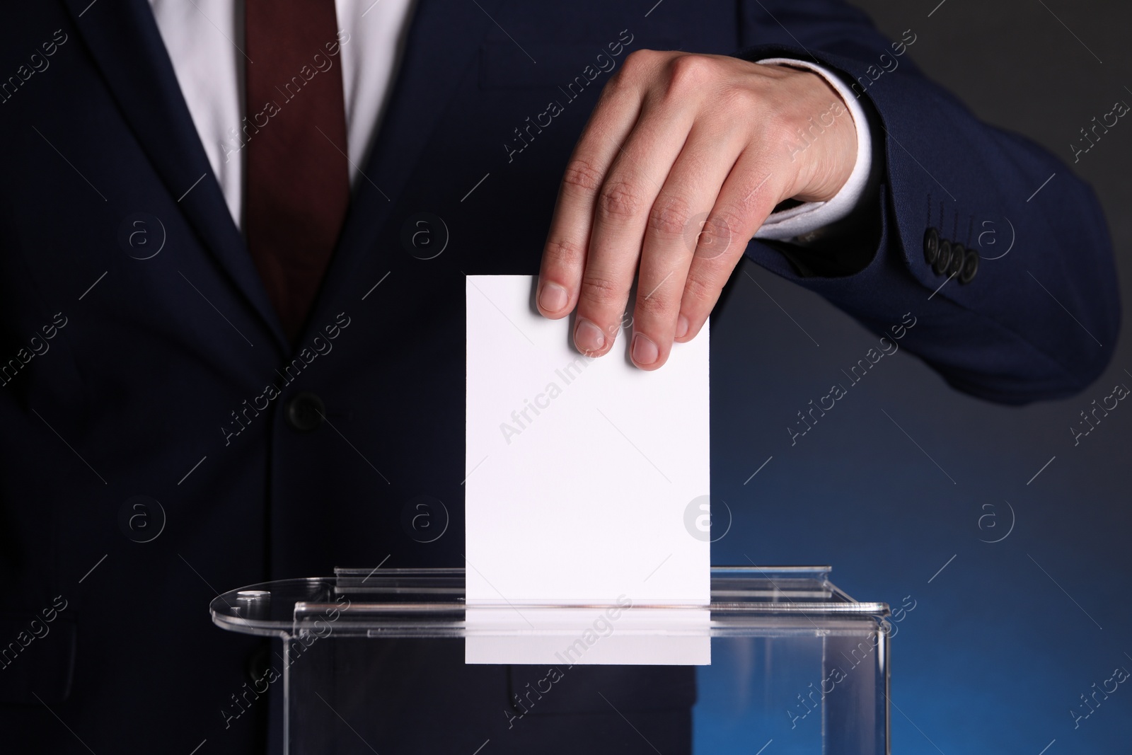 Photo of Man putting his vote into ballot box on dark blue background, closeup