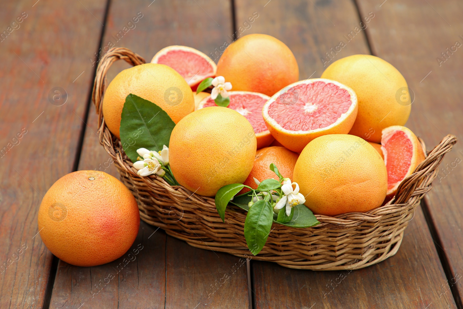 Photo of Wicker basket with fresh grapefruits and green leaves on wooden table