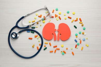 Photo of Paper cutout of kidneys, stethoscope and pills on white wooden table, flat lay