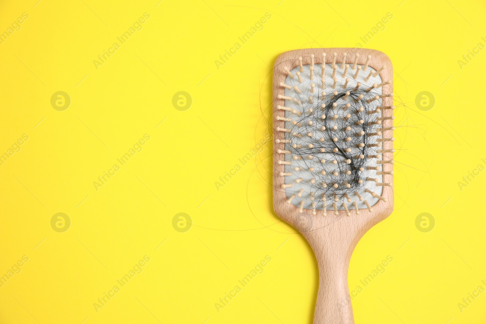 Photo of Wooden brush with lost hair on yellow background, top view. Space for text