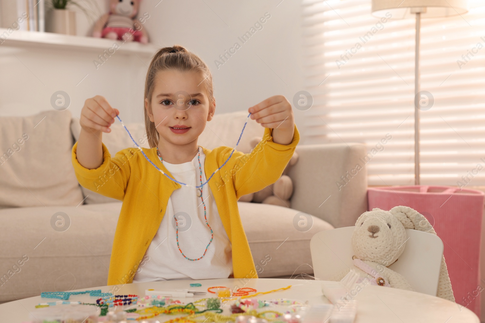 Photo of Cute little girl with beaded jewelry at table in room