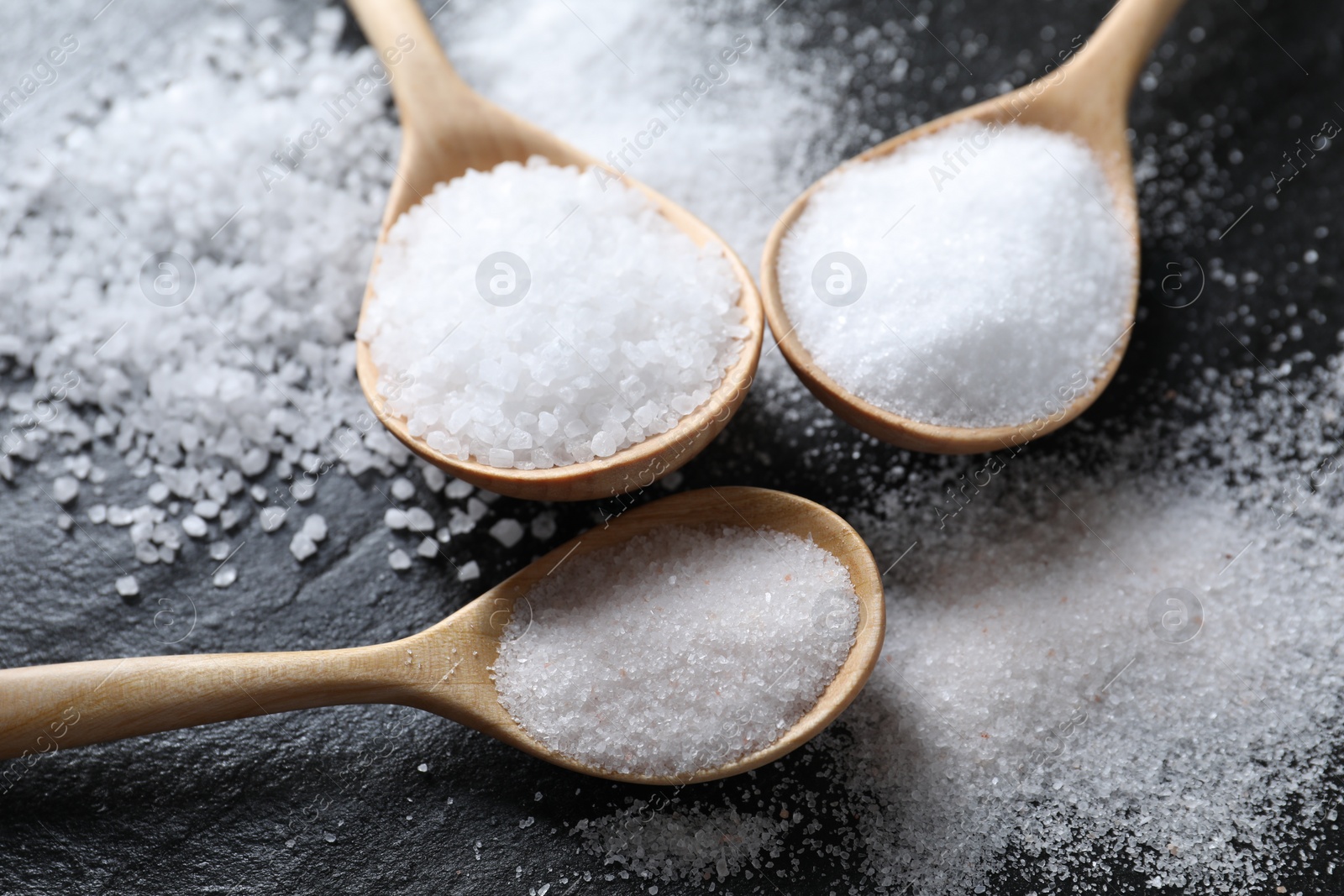 Photo of Organic salt in spoons on black table, closeup