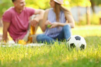 Blurred view of young couple having picnic in sunny summer park, focus on soccer ball