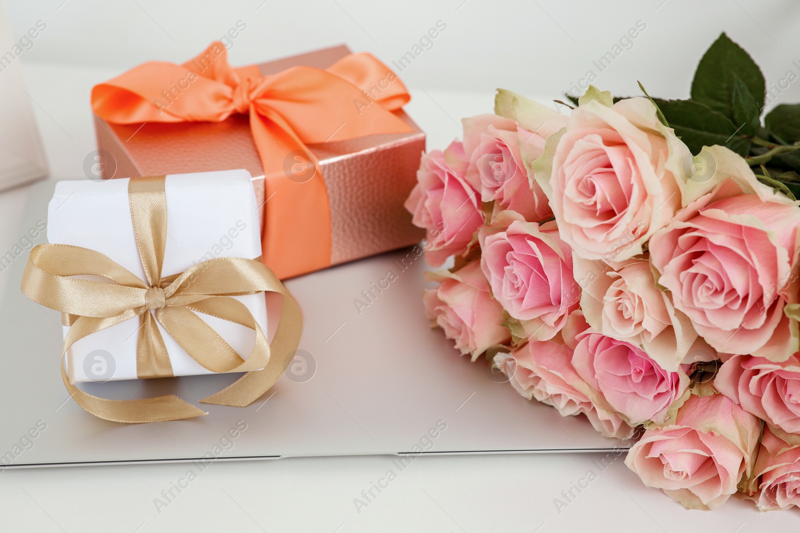 Photo of Beautiful bouquet of roses, gifts and laptop on white table. Happy birthday greetings