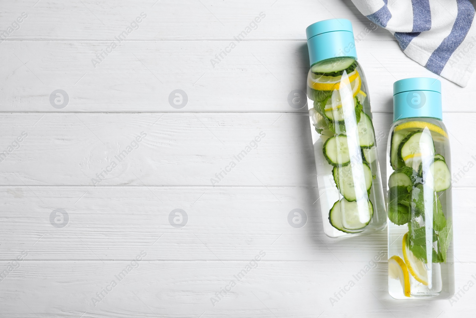 Photo of Bottles of refreshing water with cucumber, lemon and mint on white wooden table, flat lay. Space for text