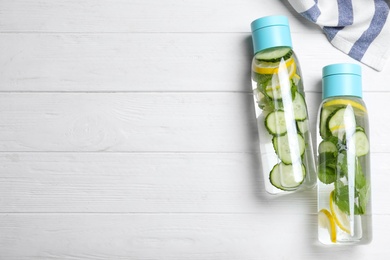 Photo of Bottles of refreshing water with cucumber, lemon and mint on white wooden table, flat lay. Space for text