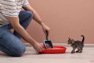 Photo of Young man cleaning cat litter tray at home, closeup