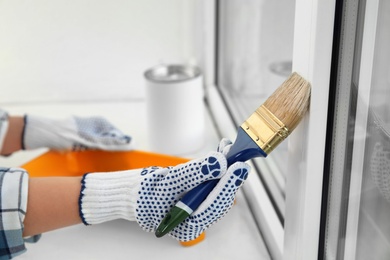 Photo of Woman painting window frame at home, closeup