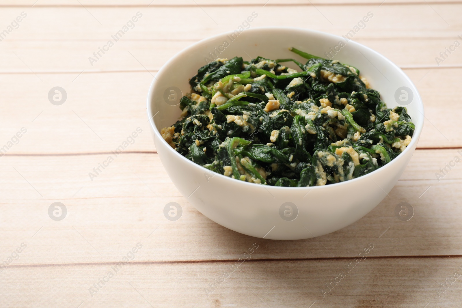 Photo of Tasty spinach dip with eggs in bowl on light wooden table, space for text