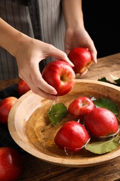 Photo of Woman washing ripe red apples in bowl of water at table, closeup