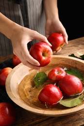 Woman washing ripe red apples in bowl of water at table, closeup