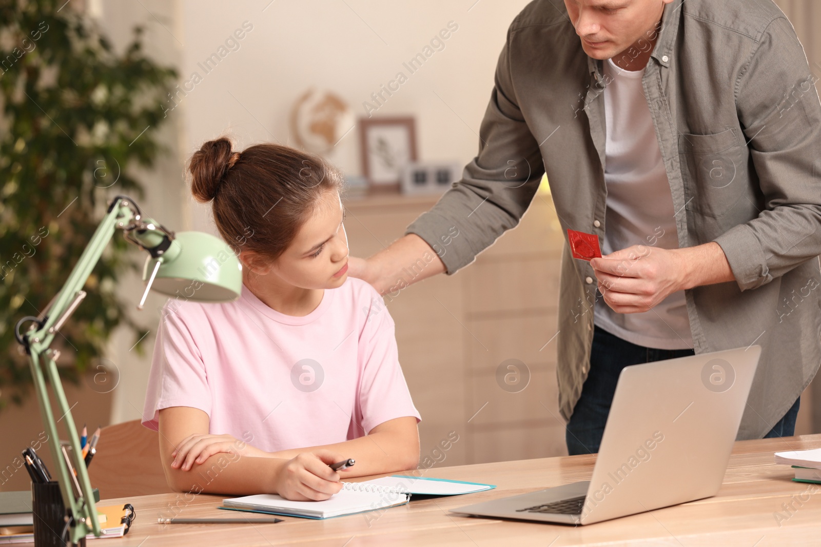 Photo of Father talking with his teenage daughter about contraception while she doing homework at home. Sex education concept