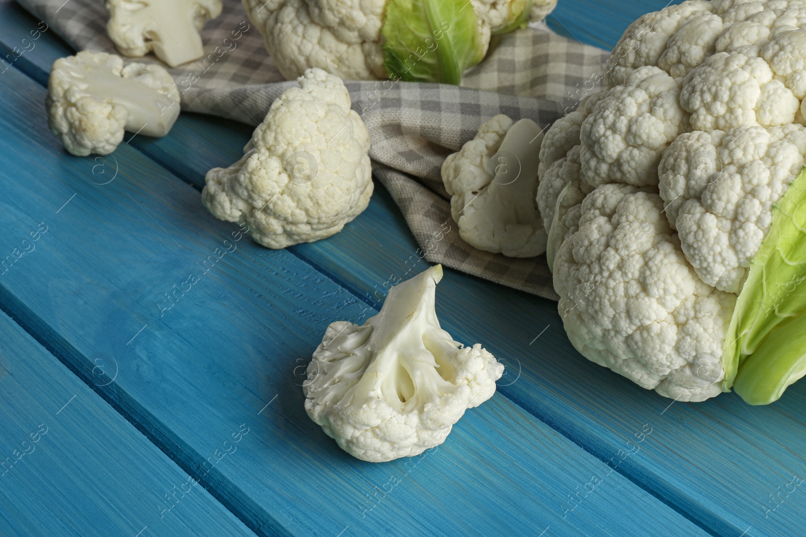 Photo of Fresh whole and cut cauliflowers on light blue wooden table, closeup