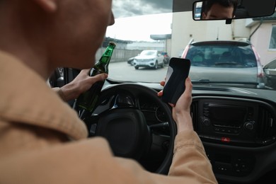 Photo of Man with bottle of beer and smartphone in car, closeup. Don't drink and drive concept