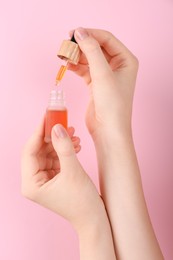 Woman holding bottle of essential oil on pink background, closeup