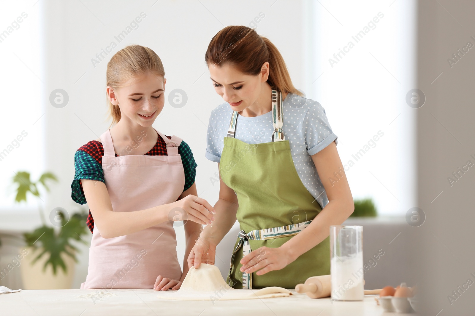 Photo of Mother and her daughter making dough at table in kitchen