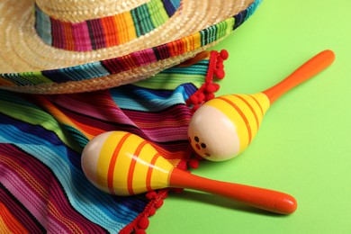 Mexican sombrero hat, poncho and maracas on green table, closeup