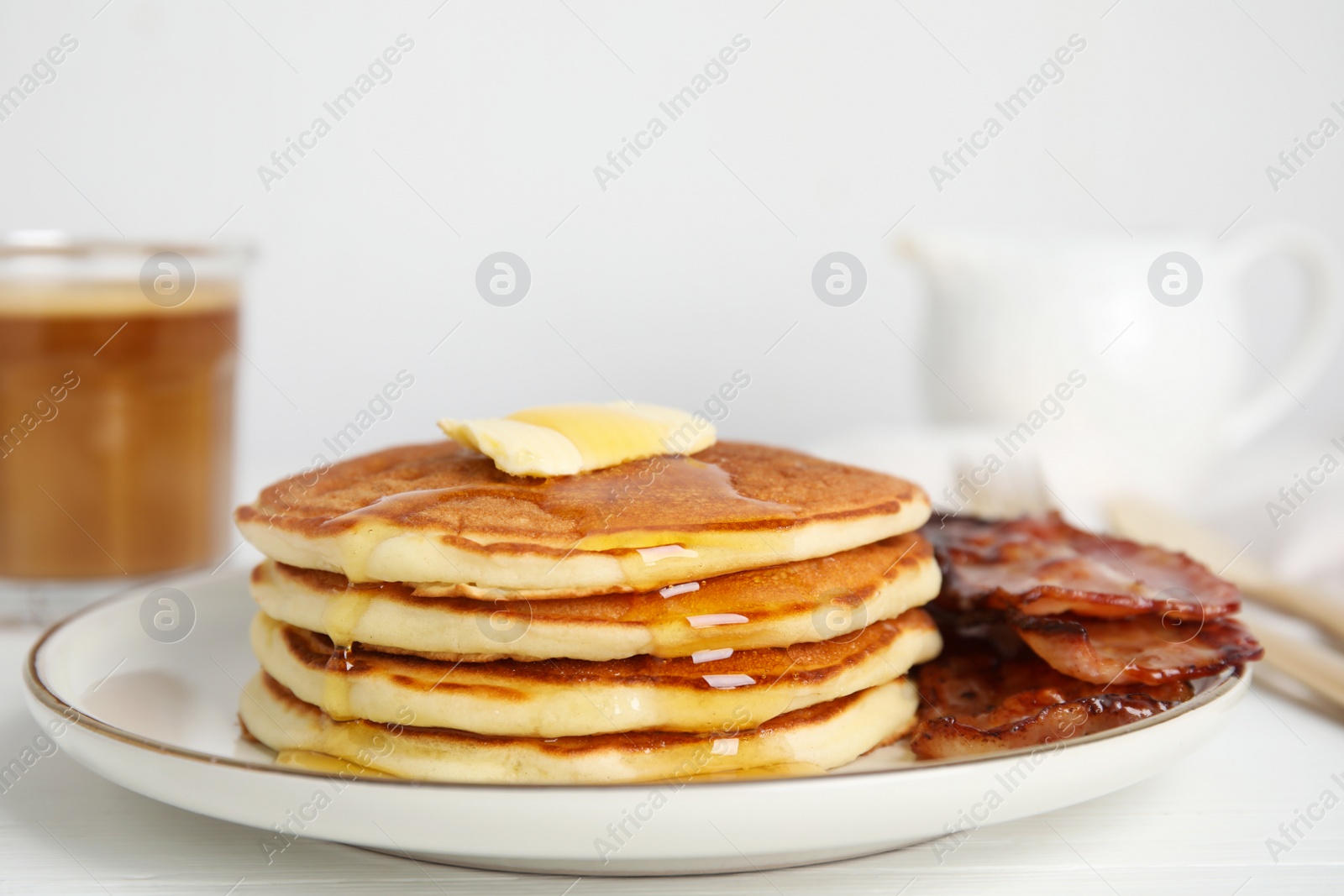 Photo of Delicious pancakes with maple syrup, butter and fried bacon on white wooden table, closeup