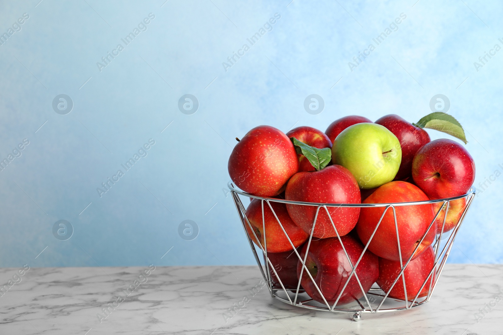 Photo of Different apple among red ones in metal basket on table. Space for text