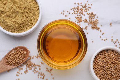 Photo of Bowl of natural oil, mustard seeds and powder on white marble table, flat lay