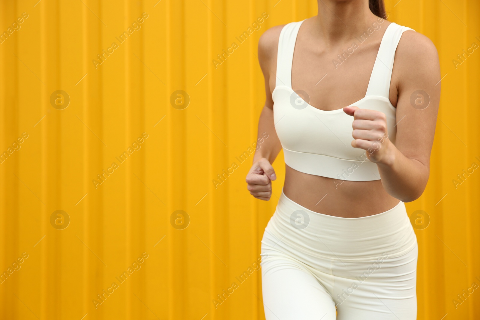 Photo of Woman in sportswear running near corrugated yellow metal wall, closeup. Space for text
