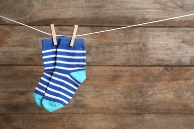 Photo of Pair of socks on laundry line against wooden background, space for text. Baby accessories