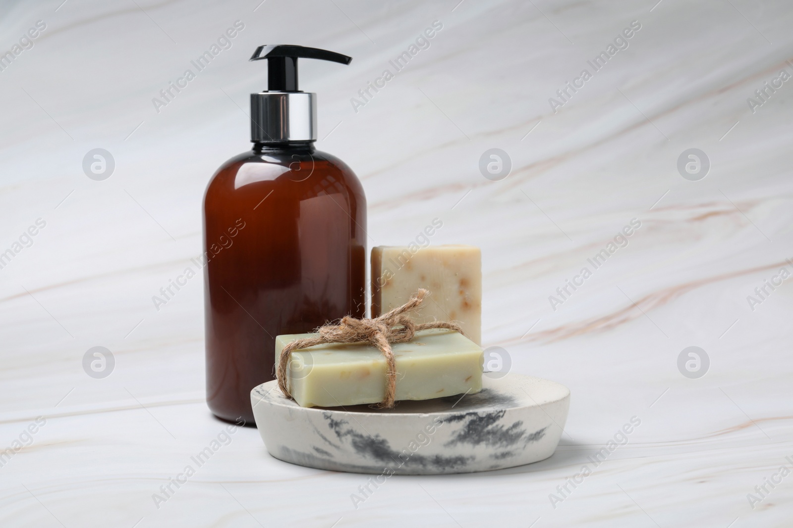 Photo of Soap bars and bottle dispenser on light marble background