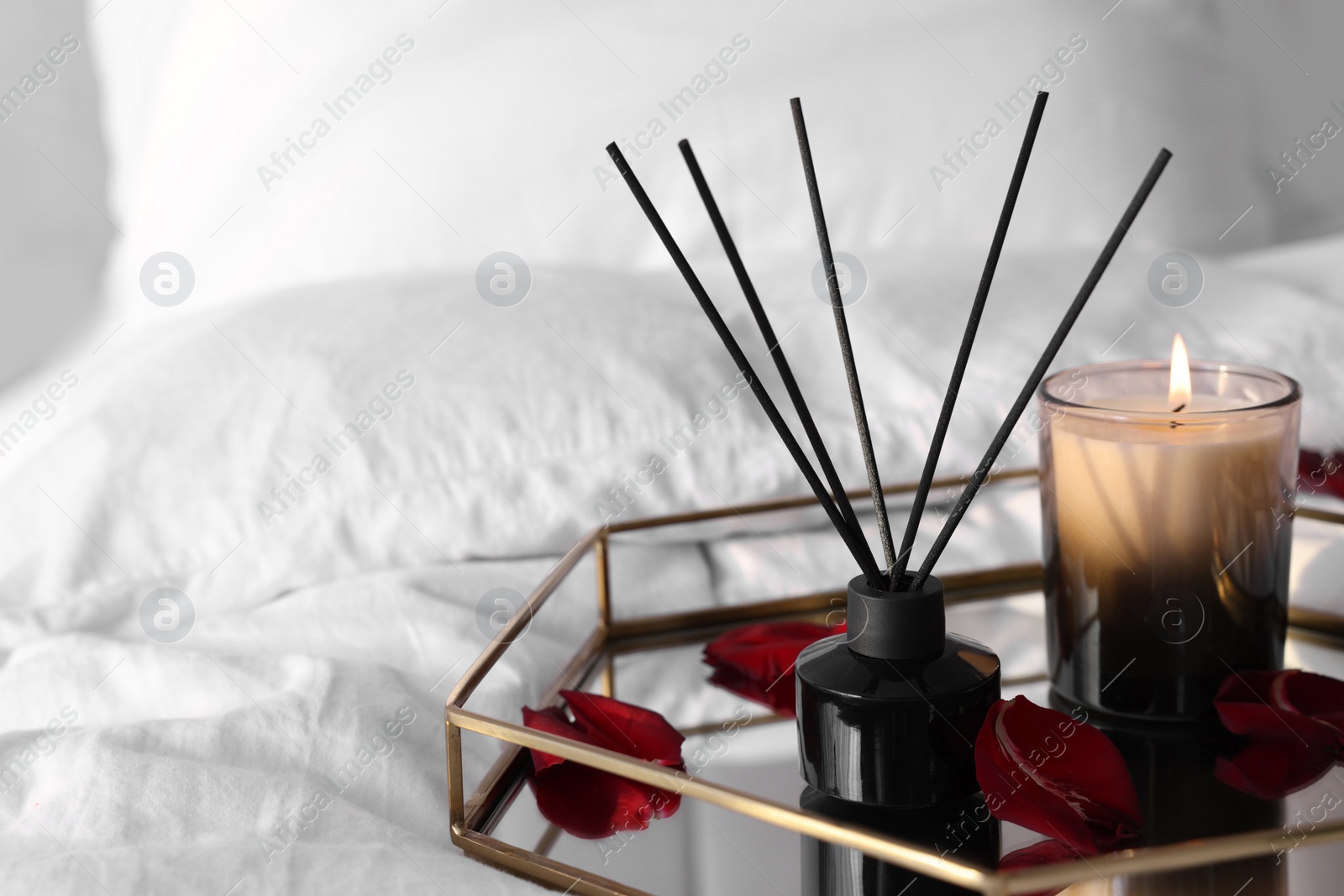 Photo of Aromatic reed air freshener, red petals and candle on bed, space for text