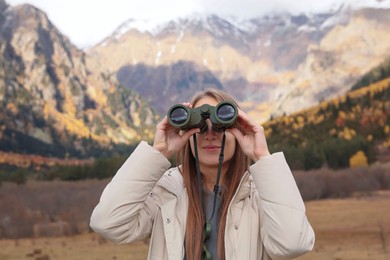 Woman looking through binoculars in beautiful mountains