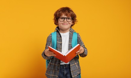 Photo of Happy schoolboy with backpack and book on orange background, space for text