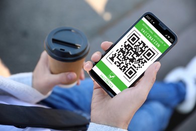 Man holding smartphone with international certificate of vaccination outdoors, closeup