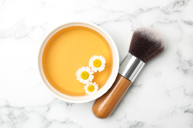 Photo of Flat lay composition with chamomile flowers and cosmetic product on white marble table