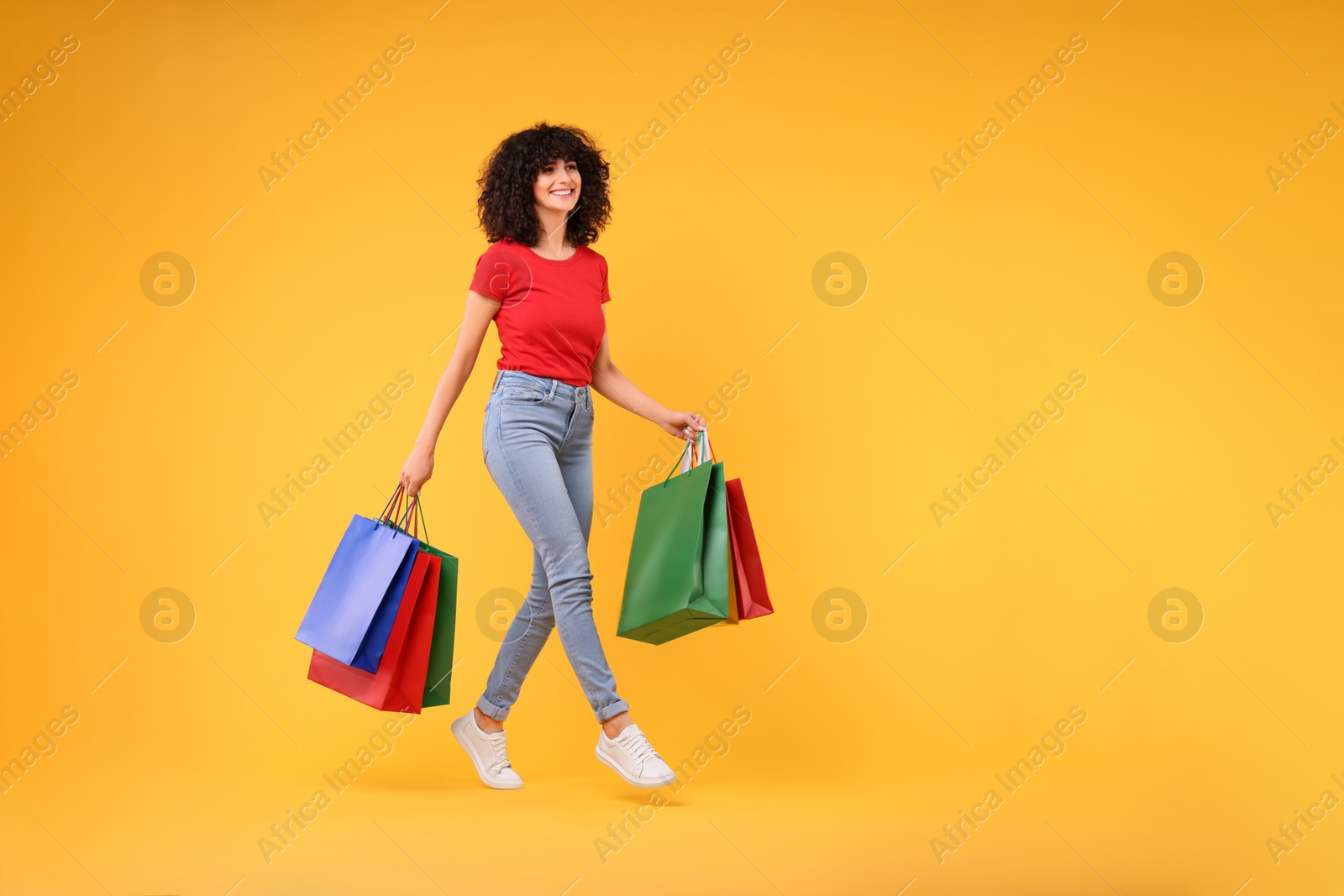 Photo of Happy young woman with shopping bags on yellow background