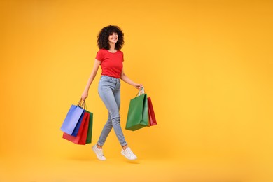 Happy young woman with shopping bags on yellow background