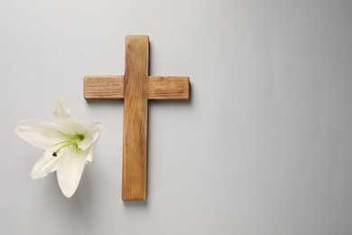 Photo of Wooden cross and lily flower on grey background, top view with space for text. Easter attributes