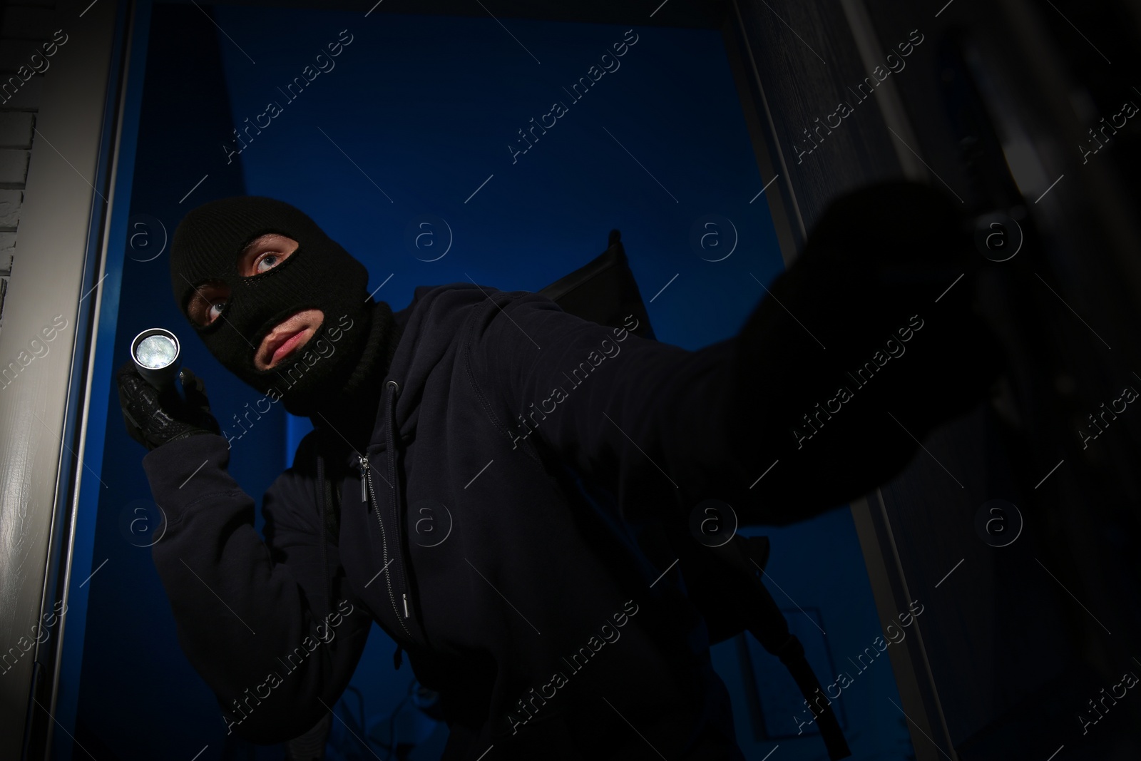 Photo of Thief with flashlight breaking into house at night