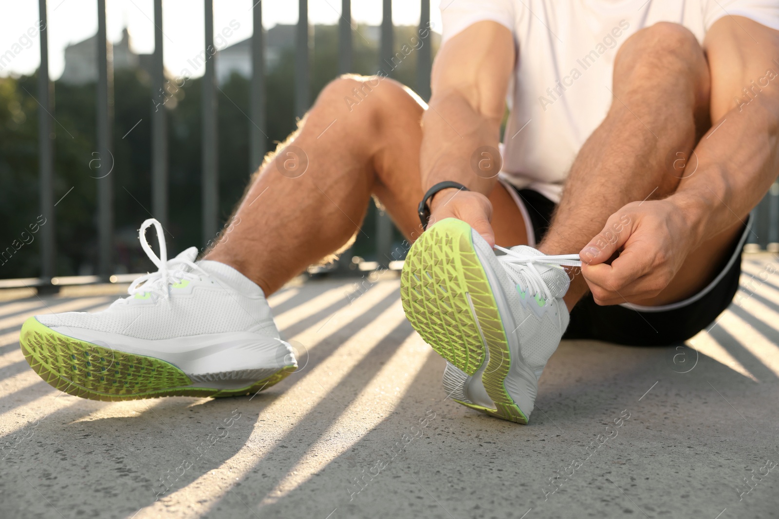 Photo of Man tying shoelaces before running outdoors on sunny day, closeup