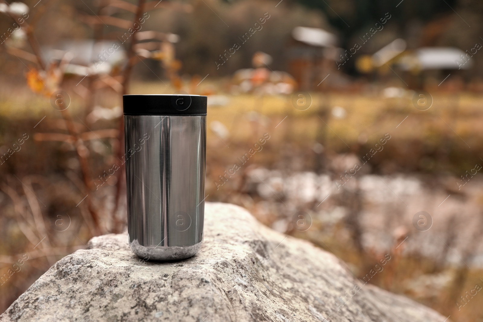 Photo of Metallic thermo tumbler on stone outdoors, space for text