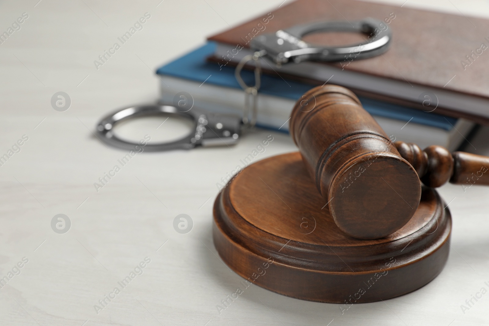 Photo of Judge's gavel, handcuffs and books on white wooden background. Criminal law concept