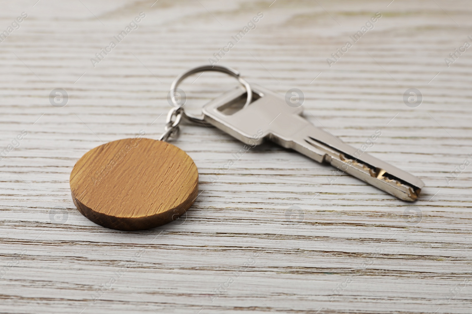 Photo of Key with keychain in shape of smiley face on light wooden background, closeup