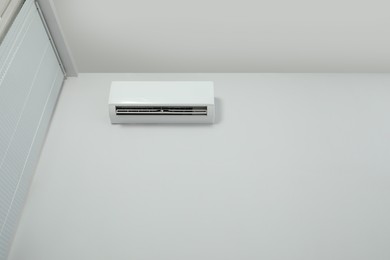 Modern air conditioner on white wall indoors, low angle view. Space for text