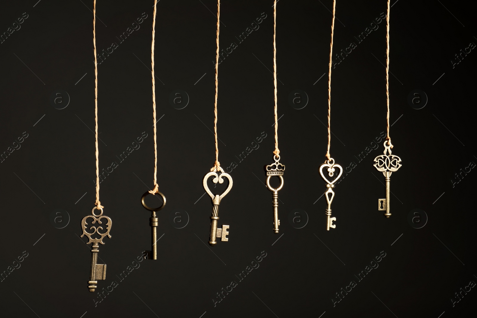 Photo of Bronze vintage ornate keys hanging on threads against dark background