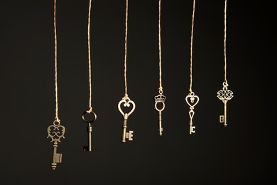 Photo of Bronze vintage ornate keys hanging on threads against dark background