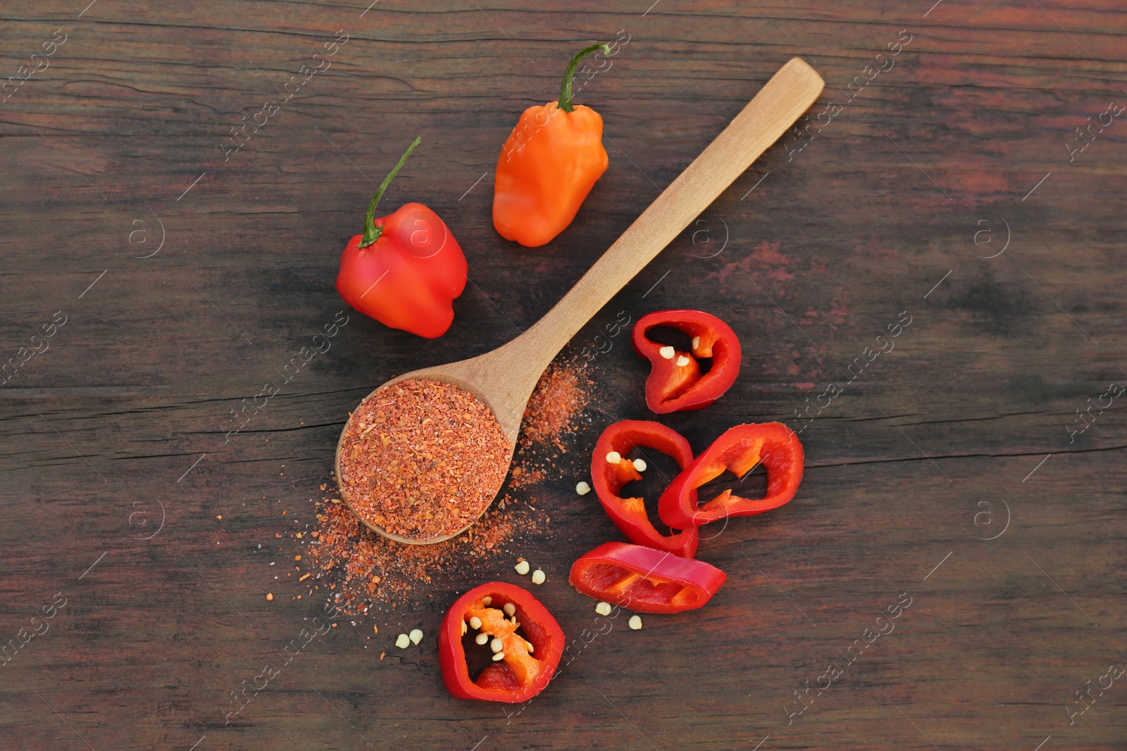 Photo of Different ripe chili peppers and spoon with spice on wooden table, flat lay